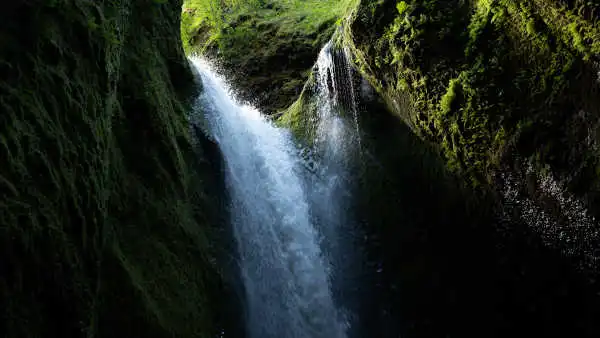 A waterfall falls from a skylight into a dark canyon