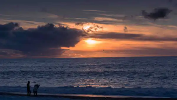 Two people are watching a beautiful sunset over a black sand beach