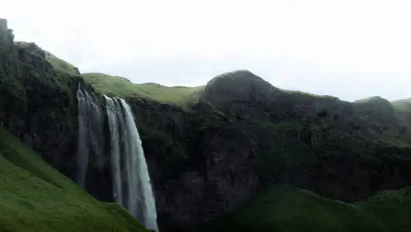 In a misty weather, among green and dark cliffs, falls a waterfall