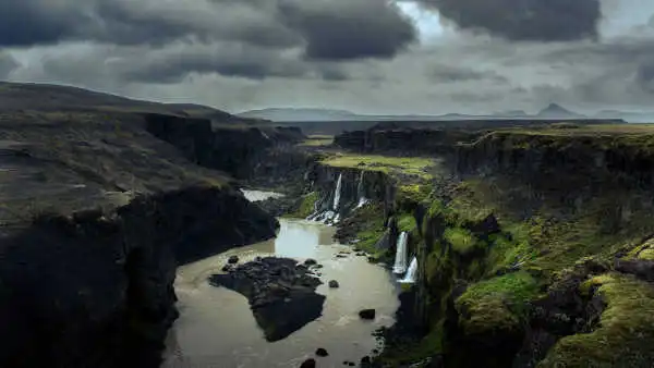 Waterfalls are falling inside of a black and green canyon