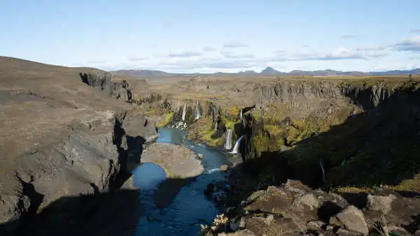 Under a bright blue sky, waterfalls are flowing down inside of a canyon, into blue waters