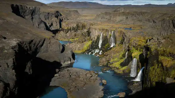 During a sunny day, many waterfalls are falling in turquoise blue waters at the bottom of a dark canyon