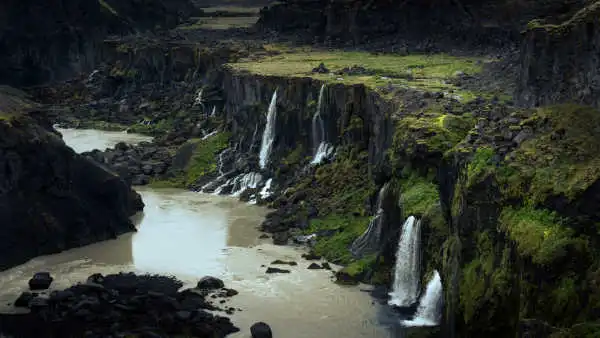 Waterfalls are falling inside of a black and green canyon