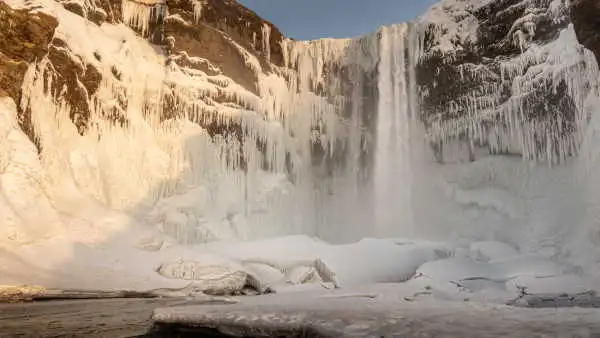 A tall waterfall is partially frozen in a wintery landscape