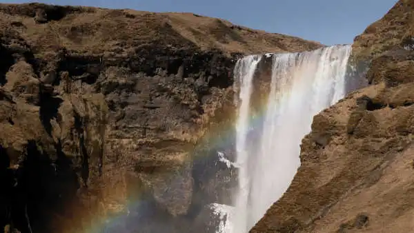 A rainbow shines in the mist of an immense waterfall