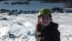 A woman with a green helmet smiles during her thrilling glacier hike