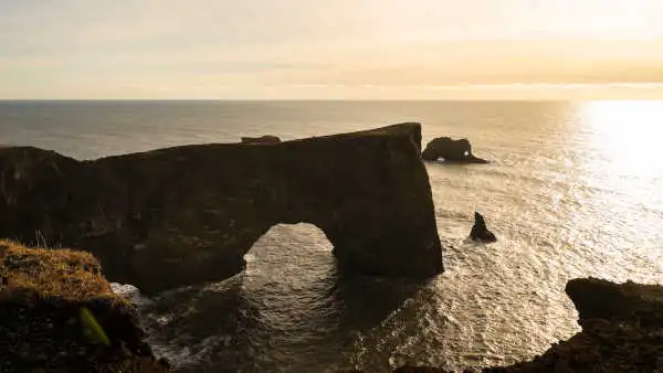 An immense stone arch dominates the ocean during sunset