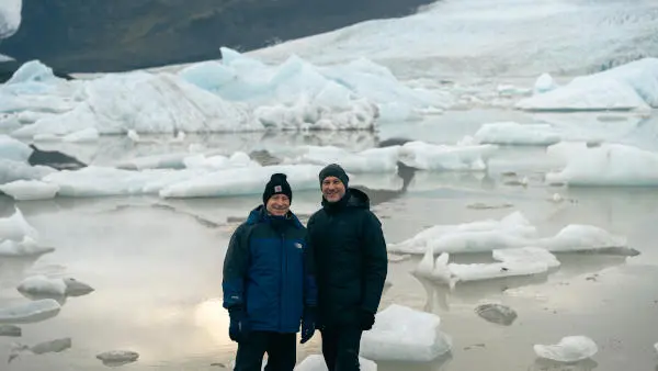 Two people are posing in front of many tiny icebergs floating on a glacier lake