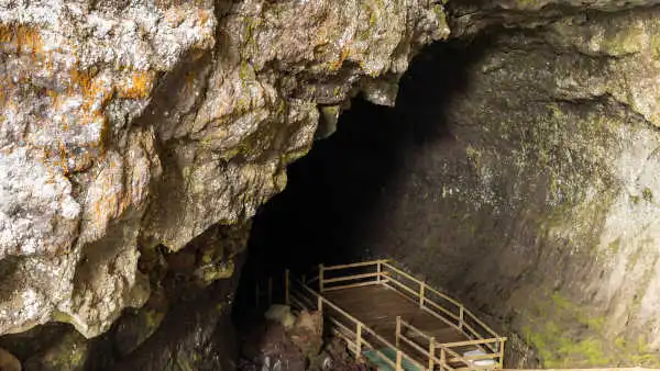 Wooden stairs are heading down inside of an immense lava cave