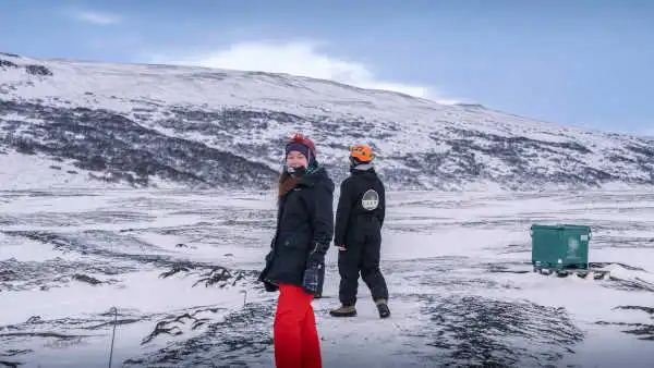 A woman and her guide, both with helmets and headlamps, are heading towards a lava tunnel during the winter