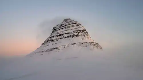 A snowy mountain summit facing pink sunrise lights