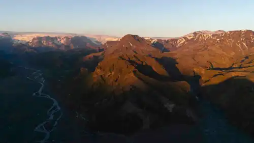 A green, lush valley with glaciers in the background, during sunset